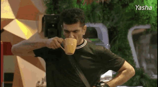a man is drinking a cup of coffee while standing in a room .