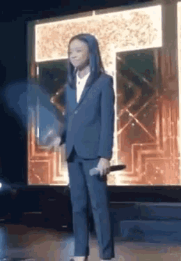 a girl in a suit is standing on a stage with a microphone .