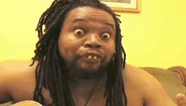 a man with dreadlocks and a beard is sitting on a couch and making a funny face .