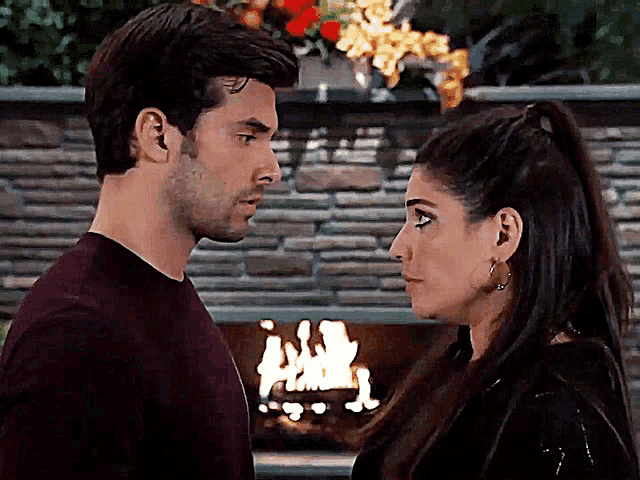 a man and woman looking at each other in front of a fireplace