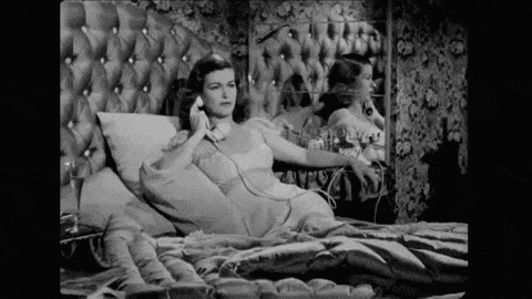 a woman is laying on a bed talking on a telephone .