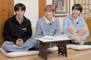 three young men are sitting on pillows next to a small table in a living room .