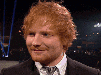 a man with red hair and a beard is wearing a black suit and tie
