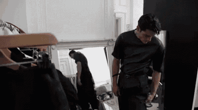 a man in a black shirt is standing in front of a mirror looking at himself .