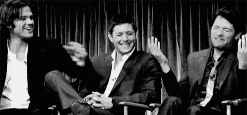 three men in suits are sitting next to each other on a stage laughing and clapping .