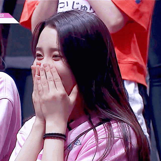 a girl covering her mouth with her hands while wearing a pink shirt that says ' ui ' on it