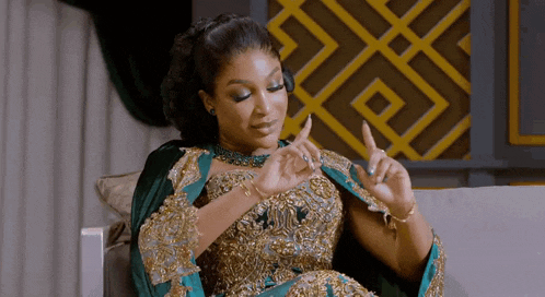 a woman in a gold and green dress is sitting on a couch and making a gesture with her hands .