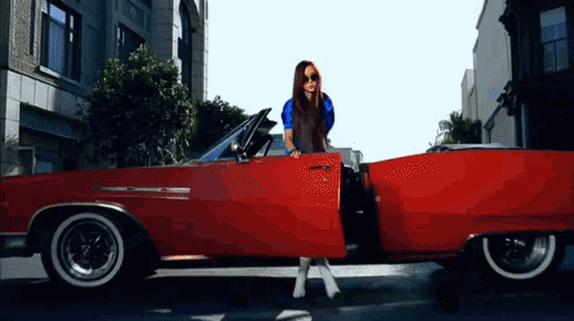 a woman is getting out of a red car with the door open