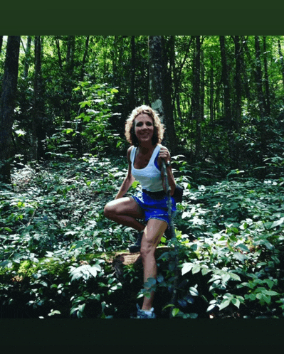 a woman is kneeling on a log in the woods
