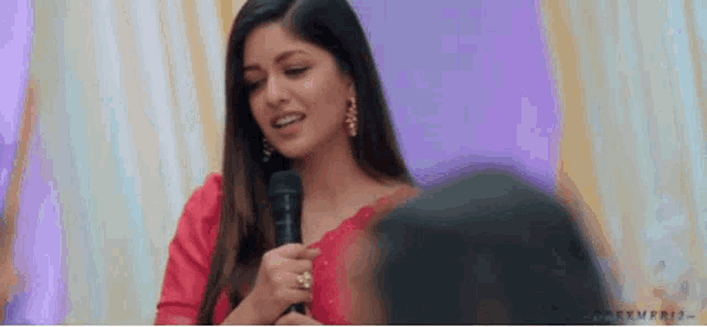 a woman in a red saree is holding a microphone in her hand .