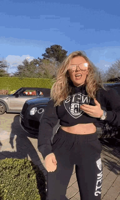 a woman wearing a crop top that says ' nba ' on it stands in front of a bentley