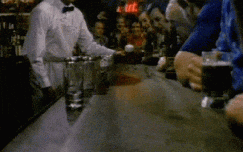 a bartender in a white shirt and bow tie is serving a drink to a group of people