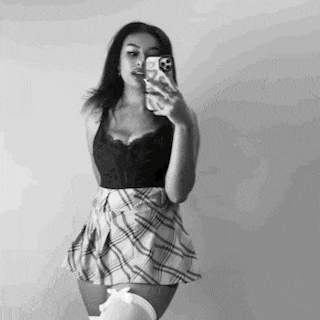 a woman in a plaid skirt is taking a selfie in a mirror .