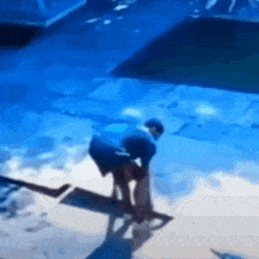 a man is kneeling down on the ground in front of a pool .