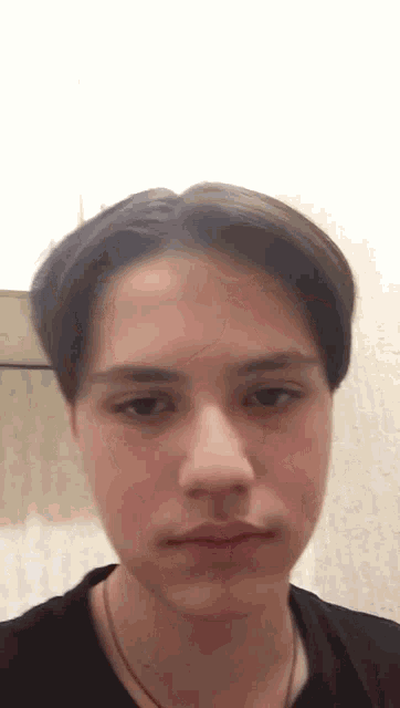 a close up of a young man 's face with a black shirt and a necklace .
