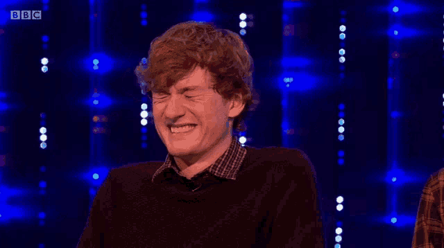 a man is laughing in front of a blue background with bbc written on it