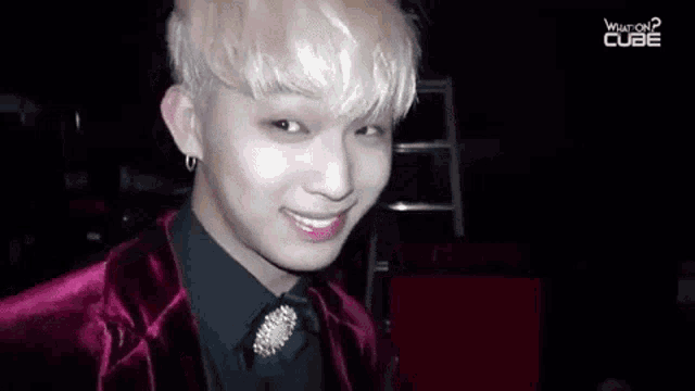 a young man with blonde hair is wearing a red velvet jacket and black shirt .