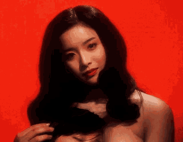 a woman without a shirt is standing in front of a red background and holding another woman 's hair .