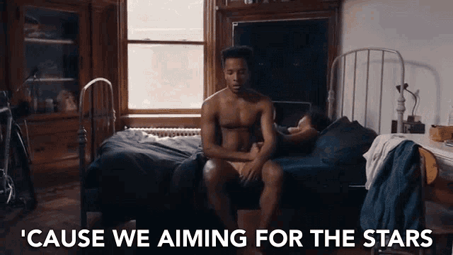 a shirtless man sits on a bed with the words ' cause we aiming for the stars ' behind him