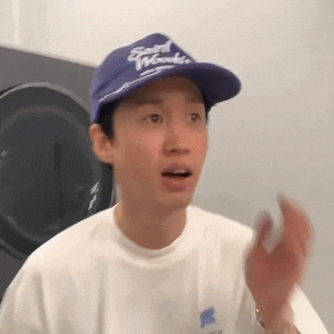 a young man wearing a purple hat and a white shirt is standing in front of a washing machine .