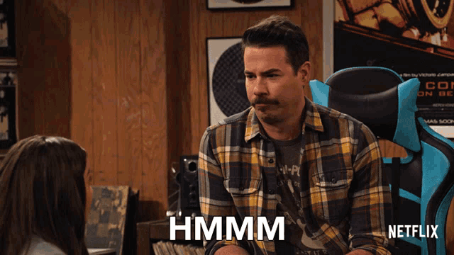 a man in a plaid shirt says hmm in front of a netflix chair