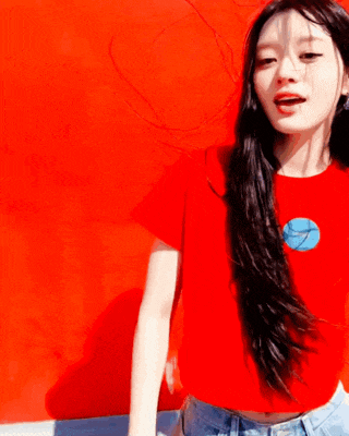 a woman wearing a red shirt with a blue circle on it is standing in front of a red wall