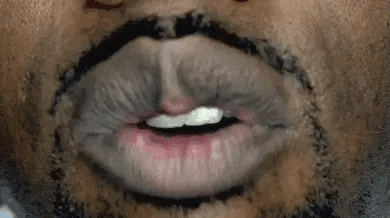 a close up of a man with a beard and mustache blowing a kiss with his mouth open .