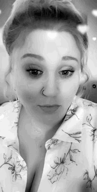 a black and white photo of a woman with a nose ring and a floral shirt .