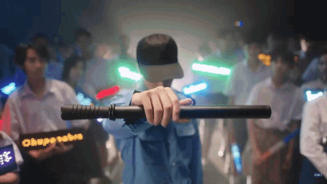 a man in a blue shirt is holding a baton in front of a crowd of people with a sign that says chape tubes