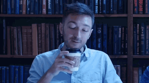 a man drinking a cup of coffee in front of bookshelves