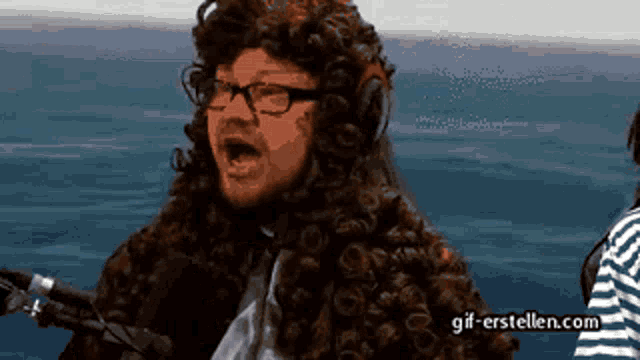 a man wearing a wig and glasses is singing into a microphone with the website gif-erstellen.com visible in the background