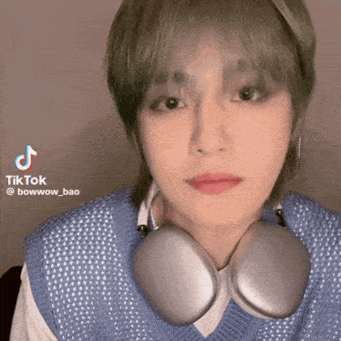a person with green hair wearing headphones and a blue vest