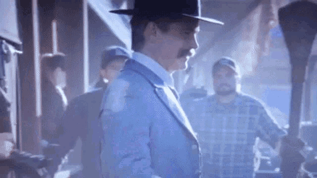 a man wearing a hat and a suit is standing in a room .