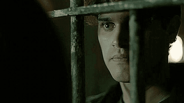 a man is behind bars in a prison cell and looking out of the bars .