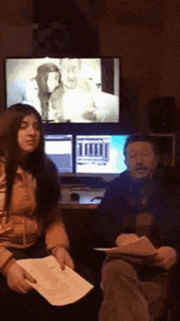 a man and a woman are sitting in front of a computer screen with a picture of a man and woman on it