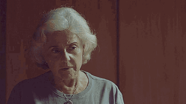 an older woman wearing a grey shirt and a necklace