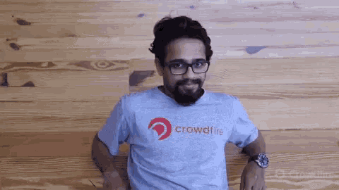 a man wearing glasses and a crowdfire shirt smiles