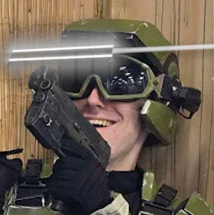 a man wearing a helmet , goggles and a gun is smiling while holding a gun .