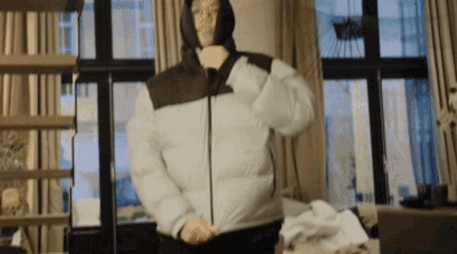 a man wearing a jacket with a hood is standing in front of a window .