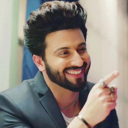 a man with a beard wearing a suit and a necklace is smiling and pointing at the camera .
