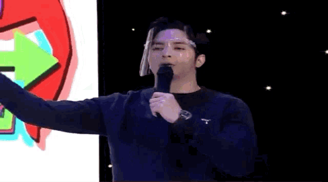 a man wearing a face shield is holding a microphone and talking into it .