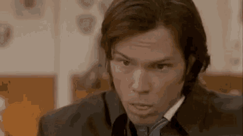 a man with long hair is wearing a suit and tie and making a funny face .
