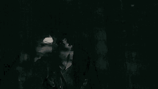 a man in a black jacket is standing in the dark looking at something .