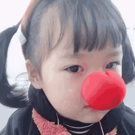 the little girl is wearing a red clown nose .