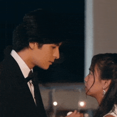a man in a tuxedo and a woman in a white dress are looking into each other 's eyes
