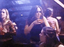 a group of women are standing in a dark room drinking alcohol