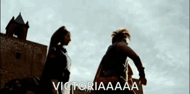 a man and a woman are standing in front of a castle and the words victoriaaaa are written on the screen