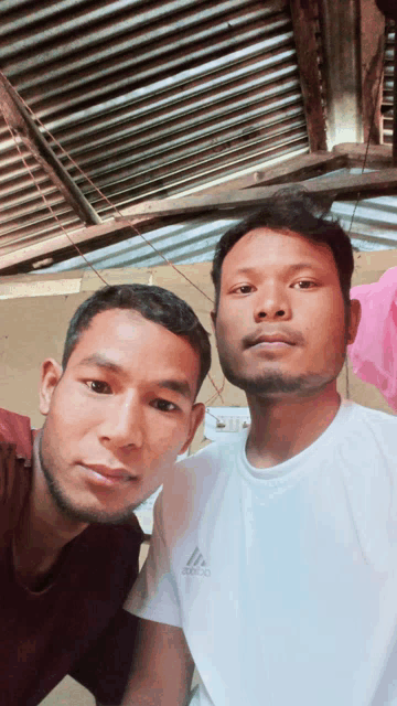 two men posing for a picture with one wearing a white adidas shirt