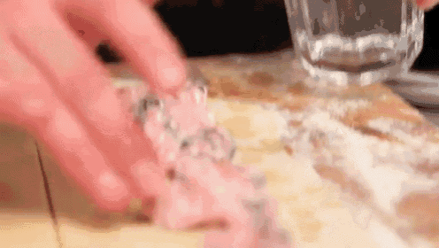 a person is holding a glass of water over a piece of meat on a cutting board .
