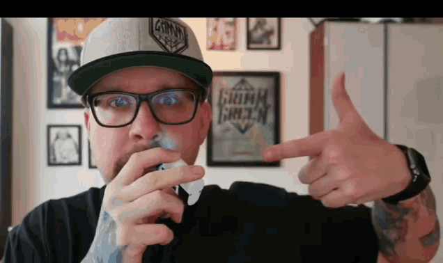 a man wearing glasses and a hat is pointing to a framed picture that says grimm green
